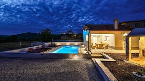 Ein modernes Haus mit Swimmingpool, Sitzgelegenheiten im Freien und einer Steinterrasse.