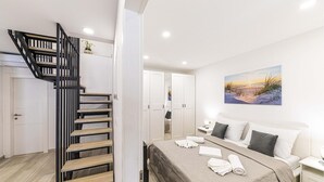 Ein Hotelzimmer mit Treppe, einem Bett mit Kissen, einem Bild mit Strandmotiv und einem Nachttisch.