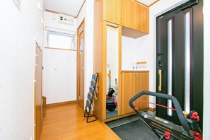 A hallway with wooden flooring, a treadmill, a door with a mirror, and a shoe rack.