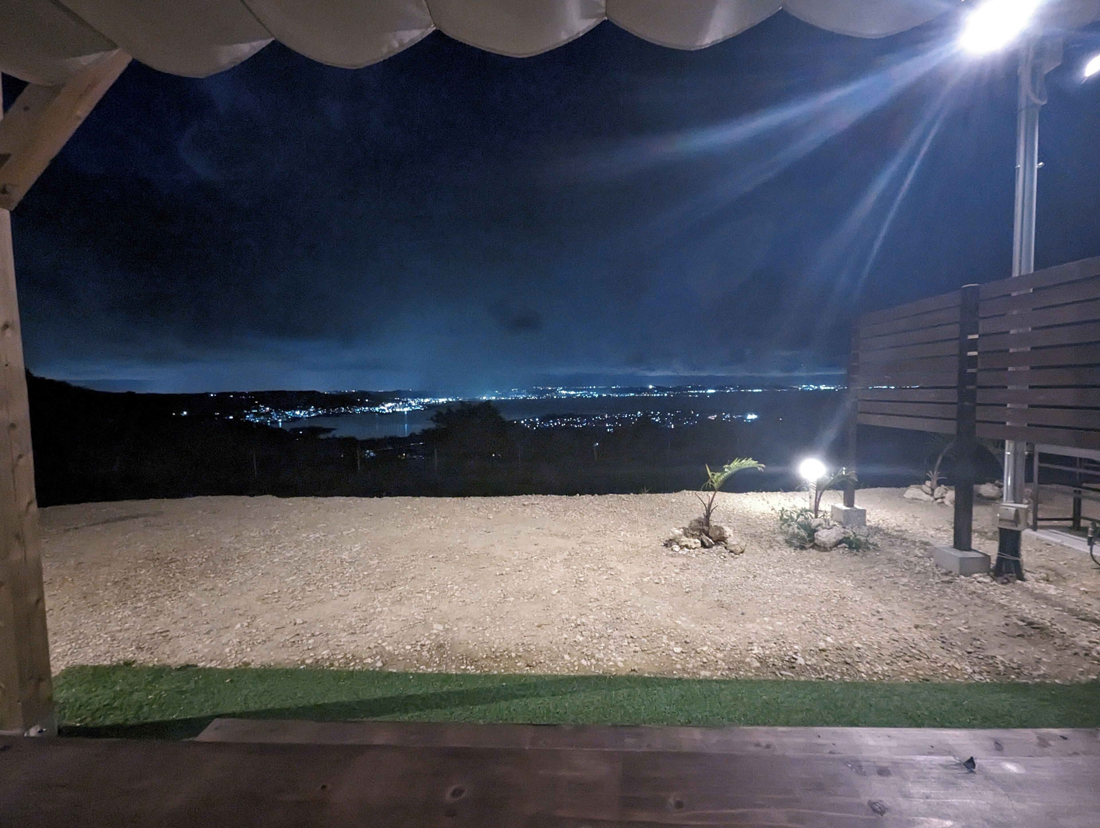 Vista nocturna des d'una zona exterior coberta amb sòl de grava, una petita planta i una banca.