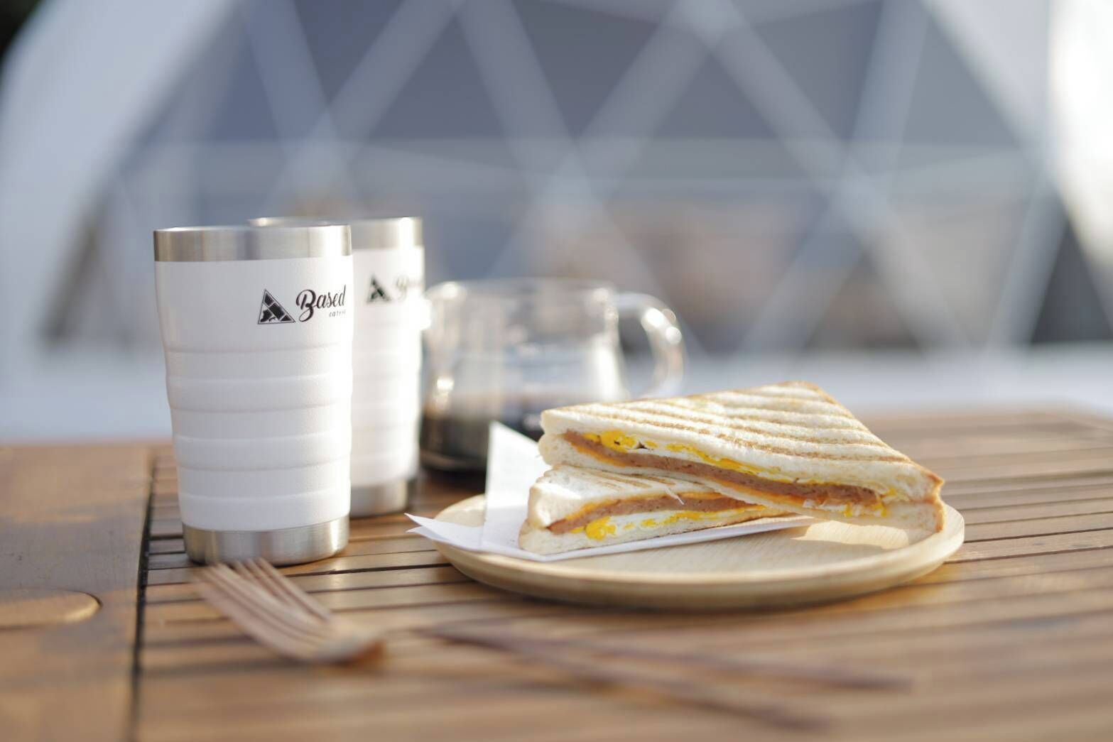 A sandwich on a plate, a cup, and a fork on a wooden table.