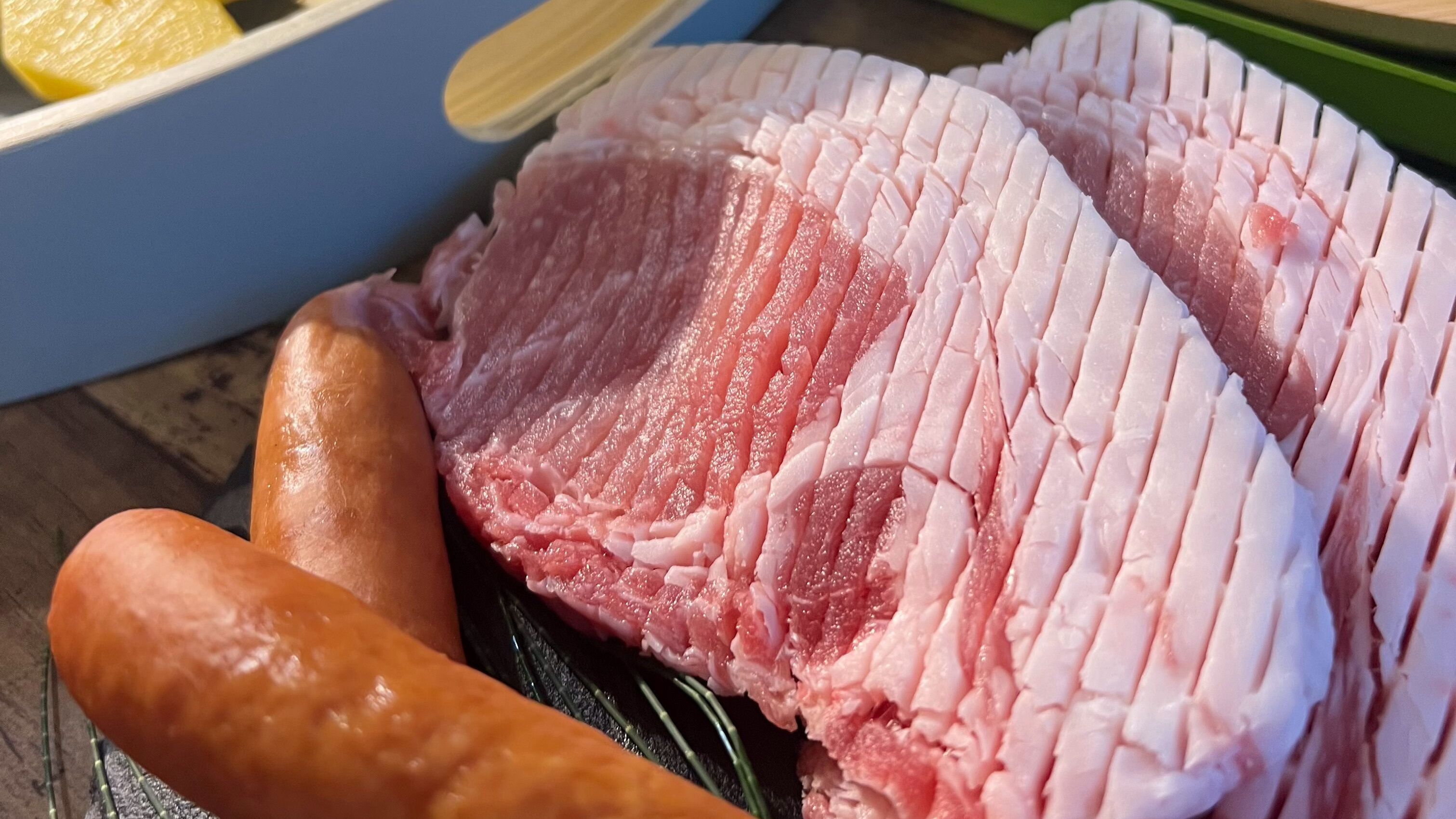 A large piece of raw meat, possibly pork, with a rib bone and a sausage on a wooden surface.