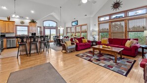 A spacious living area with a red sofa, wooden flooring, and large windows. - 7725- Sun Kissed - Avon Retreat | Pool, Hot Tub & Theater Room (Avon)