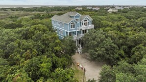 A large, two-story house surrounded by dense forest, with a visible front porch and a staircase leading to the second floor. - 7725- Sun Kissed - Avon Retreat | Pool, Hot Tub & Theater Room (Avon)