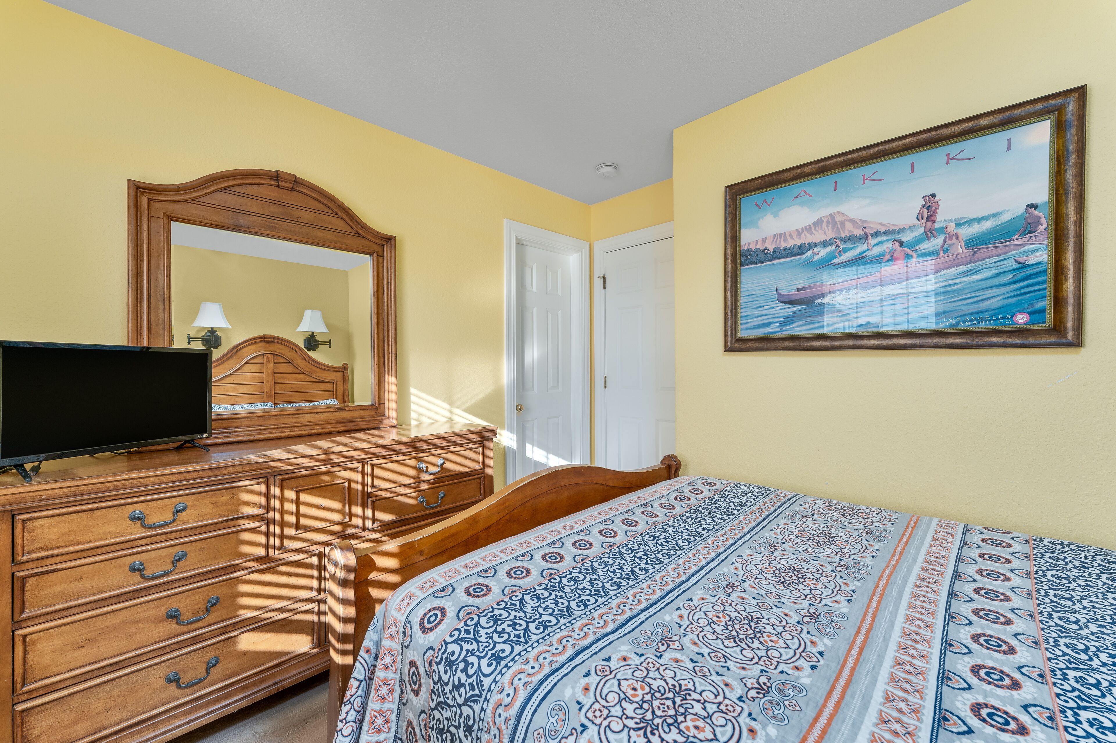 A hotel room with a bed, a dresser, a television, a painting, and a door.