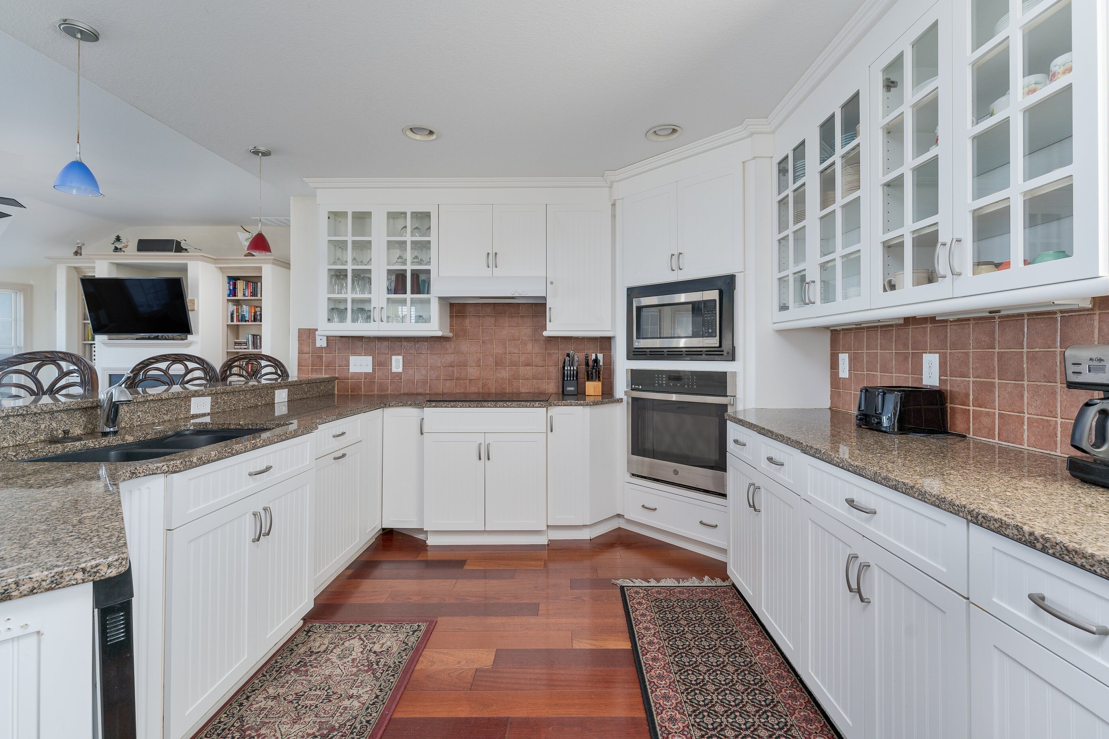 A modern kitchen with white cabinetry, granite countertops, a built-in microwave, and an oven.