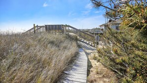 En træpromenade der fører til et strandhus med et træhegn og trapper.