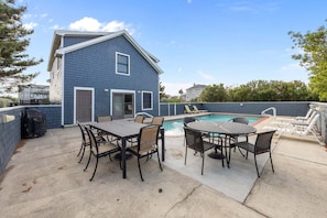 Un jardin à l’arrière d’une maison, avec une piscine, du mobilier de jardin et une maison dont la façade est bleue.