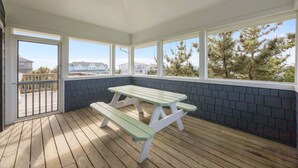 Un espacio al aire libre cubierto con una mesa de picnic y bancos, ventanas amplias y vistas a casas y árboles.