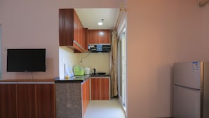 A compact kitchen with wooden cabinets, a built-in microwave, and a refrigerator. - RUJIA CONDOTEL CORP. (Lapu-Lapu)