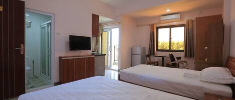 A hotel room with two beds, a TV, a desk, and a window with curtains.