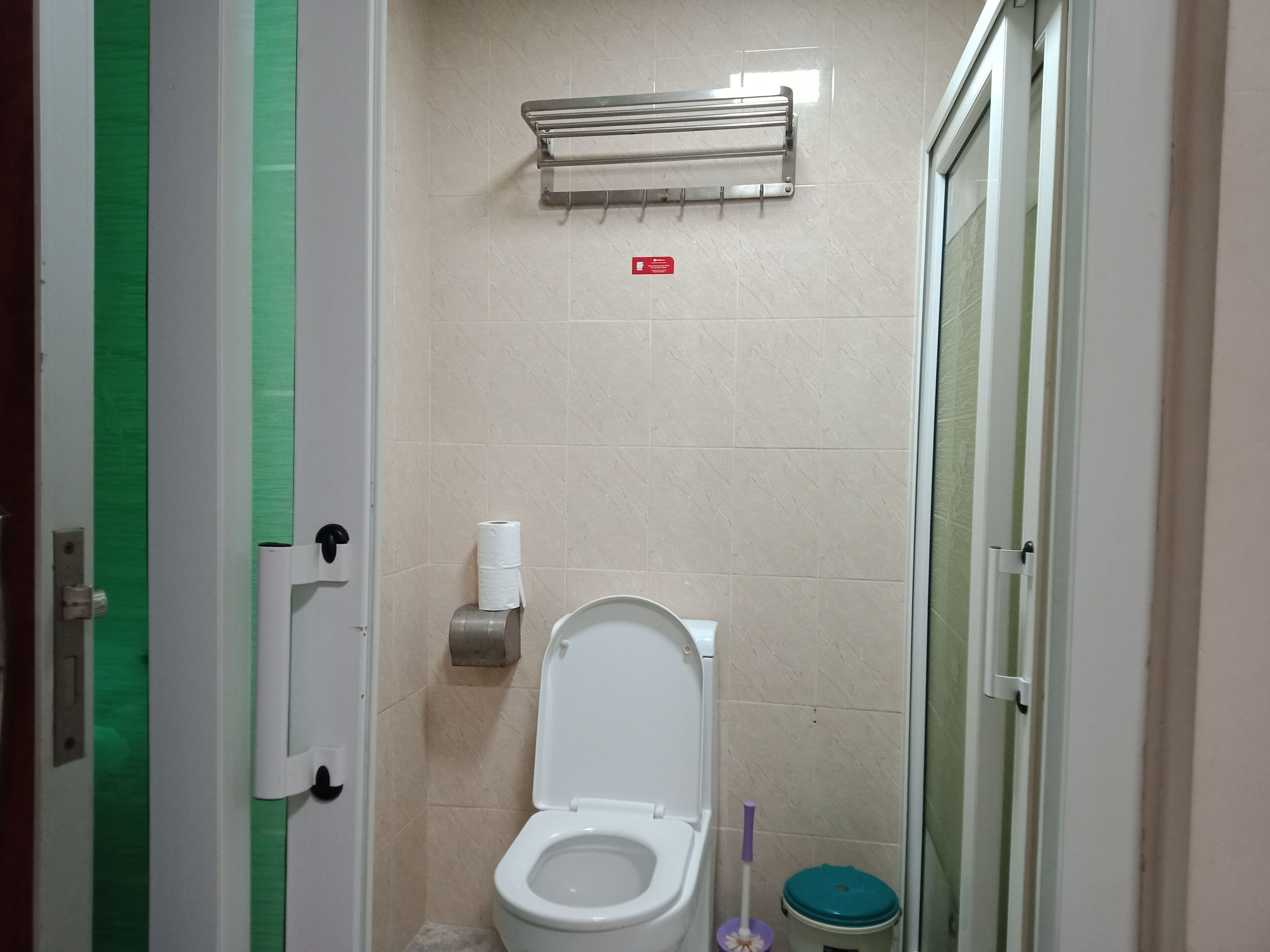 A bathroom with a toilet, a paper towel dispenser, a hand dryer, and a trash bin.