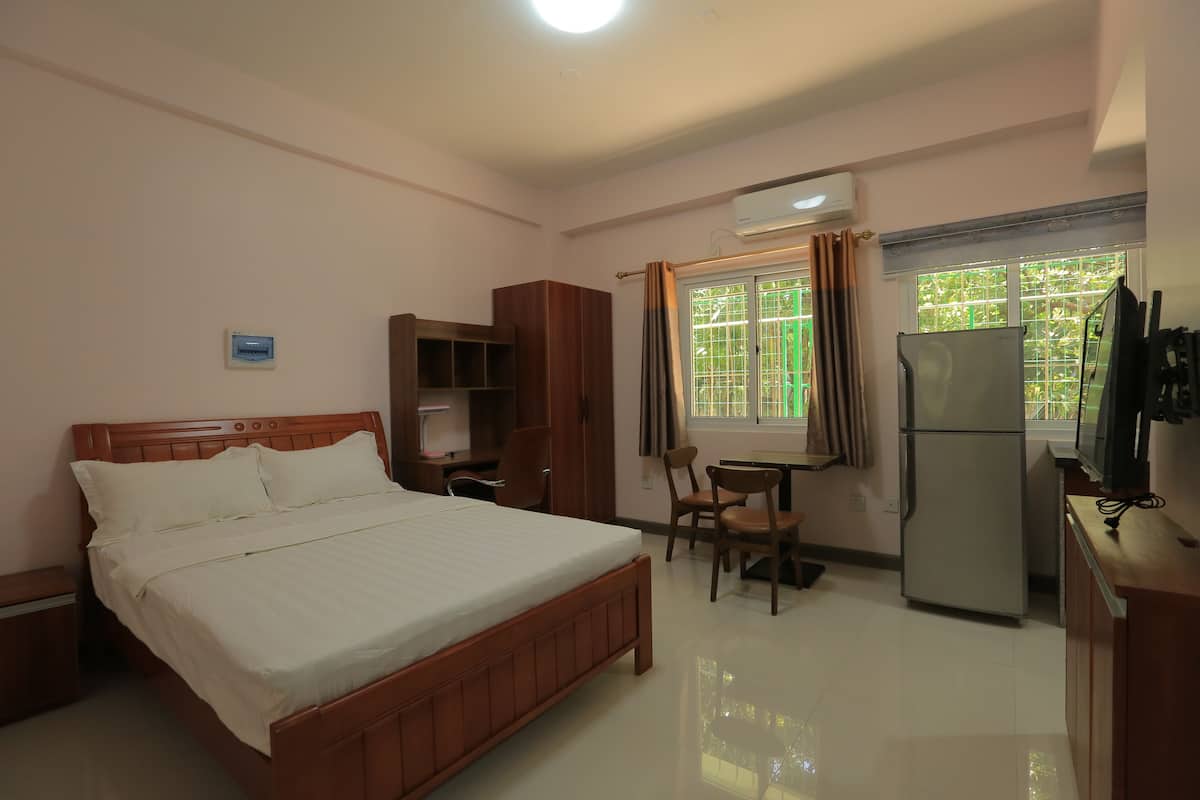 A hotel room with a bed, a desk, a chair, a refrigerator, and a window with curtains.