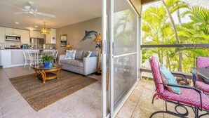 A modern kitchen with white cabinets, a dining area with a glass table, and a balcony with outdoor furniture. - Ground floor, oceanview, updated coastal style 1 bedroom gem, AC, walk to beach (Kihei)