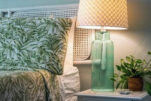 Ein Bett mit blattbedecktem Überwurf, eine Nachttischlampe, eine grüne Glasflasche und ein Topfpflanze.