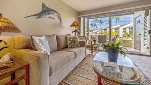 A living room with a sofa, a glass coffee table, and a wall-mounted lamp. - Ground floor, oceanview, updated coastal style 1 bedroom gem, AC, walk to beach (Kihei)