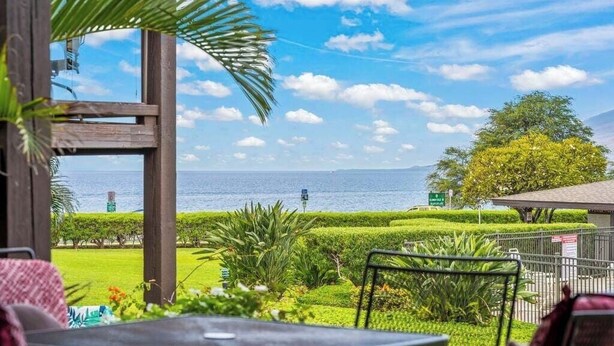 A view from a balcony with a table and chairs, overlooking a well-maintained garden and the sea. - Ground floor, oceanview, updated coastal style 1 bedroom gem, AC, walk to beach (Kihei)