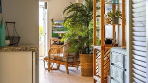 A room with a dining area, a large potted plant, a television, and a cabinet with decorative items. - Ground floor, oceanview, updated coastal style 1 bedroom gem, AC, walk to beach (Kihei)
