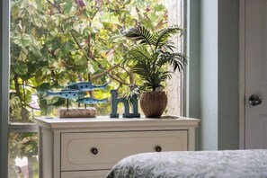 A room with a window, a dresser, a bed, and a view of trees outside.
