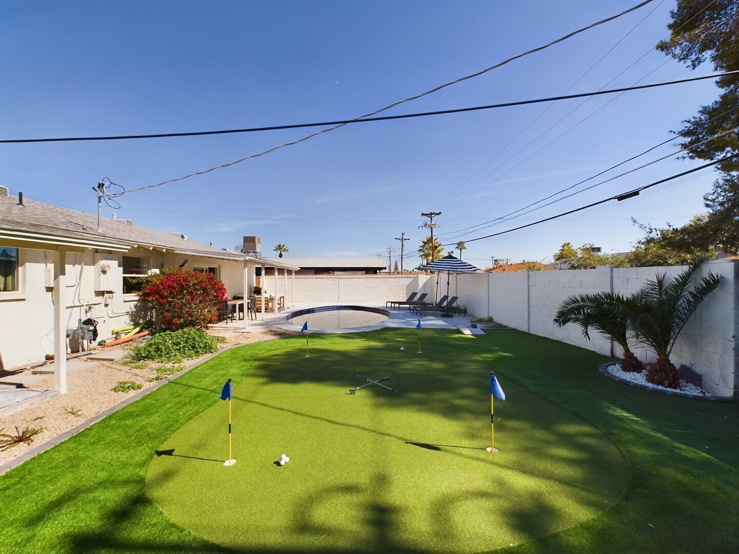 A residential property with a backyard featuring a putting green, a patio area, and a white fence.