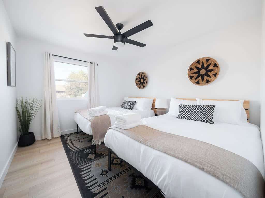 A bedroom with two beds, a ceiling fan, a window with curtains, and decorative wall art.