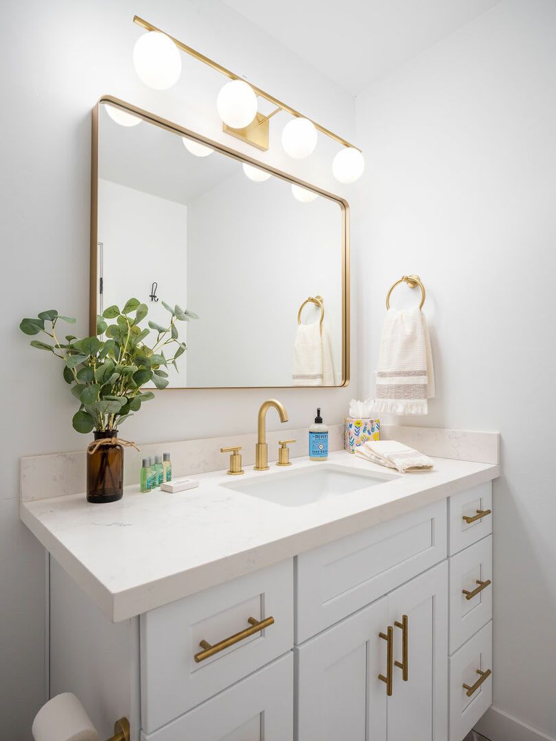 A bathroom with a large mirror, two sinks, a potted plant, and a towel rack.