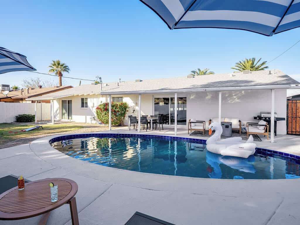 Ein Schwimmbad mit einer Schwane als Schwimmpflege, eine Terrasse mit Stühlen und ein überdachter Bereich mit Tischen und Sonnenschirmen.