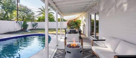 A covered outdoor area with a pool, a fire pit, and a seating area.