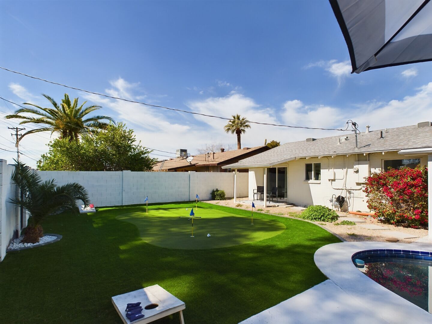 A backyard with a pool, a patio, and a house.