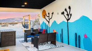 A room with a view of a desert landscape, a hammock, wicker furniture, and a wall mural. - NEW! HotTub, Hammock, FirePit, BBQ & Paved Driveway (Joshua Tree)