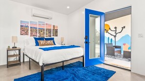 A bedroom with a bed, a blue rug, a nightstand, a lamp, and a wall with three framed pictures. - NEW! HotTub, Hammock, FirePit, BBQ & Paved Driveway (Joshua Tree)