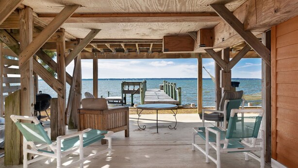 Une terrasse en bois offrant une vue sur la mer, équipée d’un barbecue, de chaises longues et d’une table.
