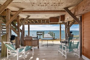 A wooden deck with a view of the sea, featuring a grill, lounge chairs, and a table. - OBX soundfront, private pier, 5 min to beach, easy to kayak & paddleboard (Nags Head)