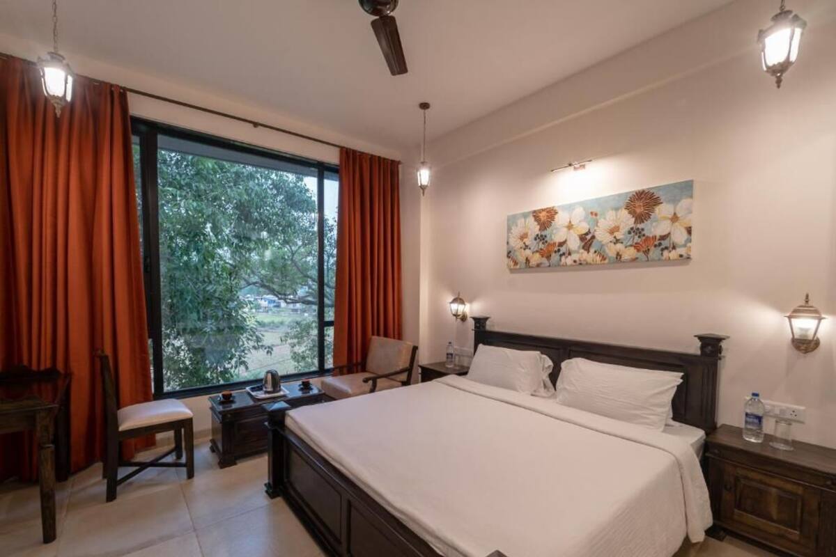 A hotel room with a large bed, a desk, a chair, a window with curtains, and a painting on the wall.