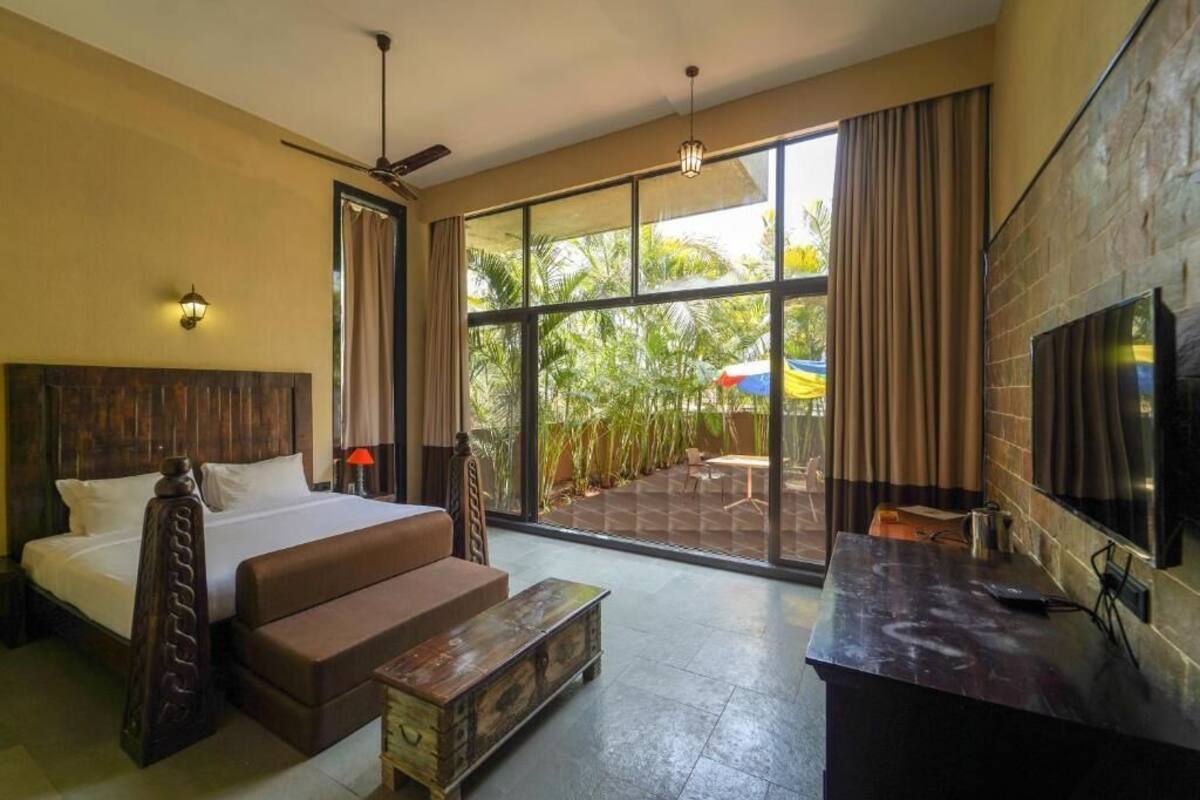 A hotel room with a bed, a sofa, a desk, a TV, and large windows with curtains.
