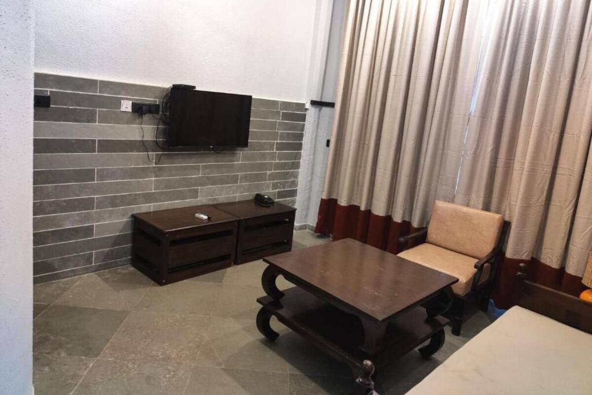 A room with a TV mounted on a brick wall, a dark wooden coffee table, a beige sofa, and a curtain.