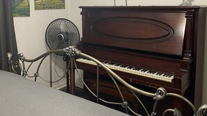 Ein Zimmer mit Klavier, Ventilator und Fernseher an der Wand.
