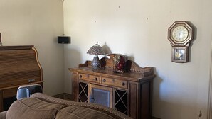 Ein Wohnzimmer mit einem braunen Sofa, einem hölzernen Beistelltisch mit Dekoration, einer Wanduhr und einem Deckenlüfter.