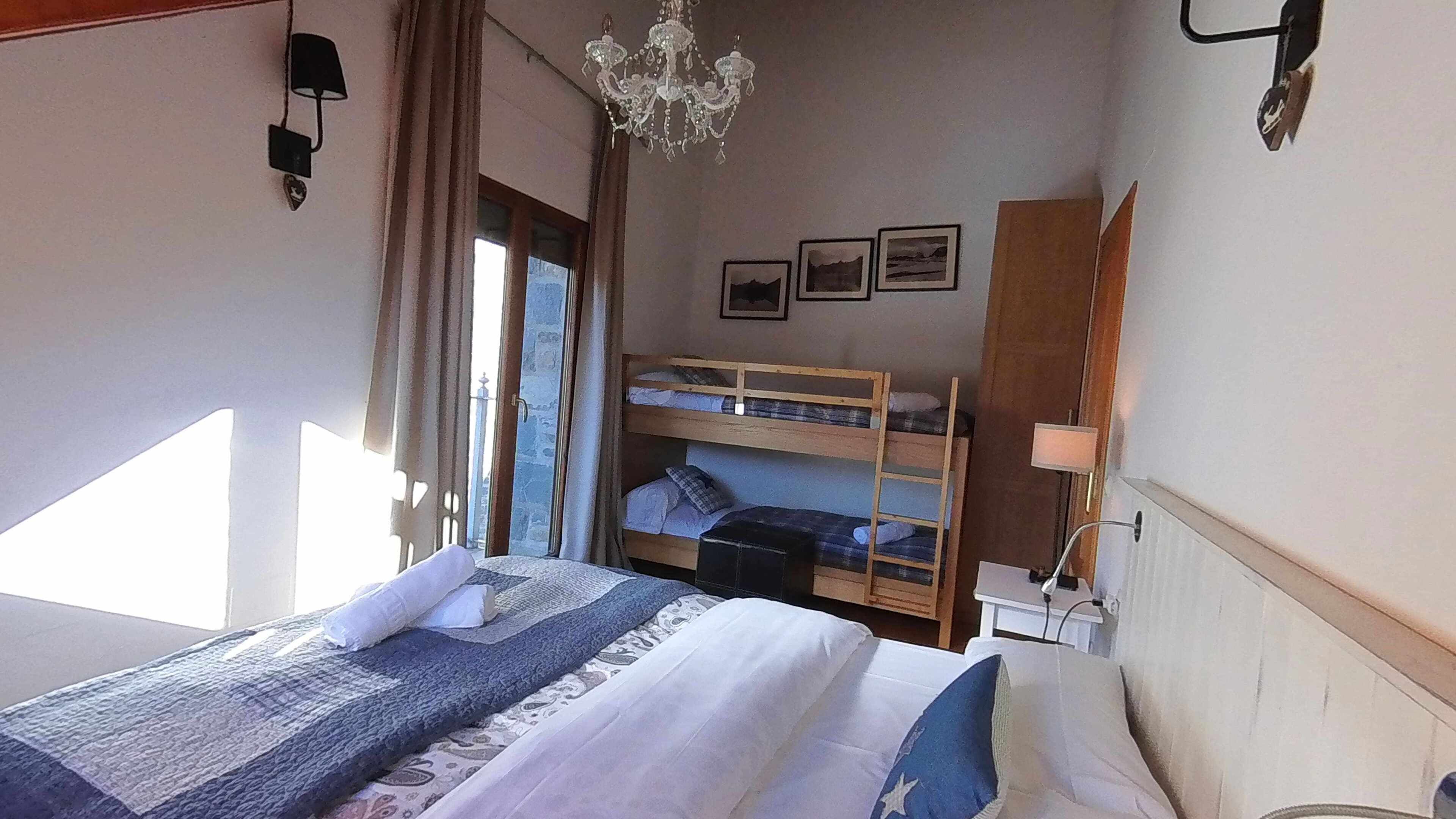 Un dormitorio con literas, un candelabro, una ventana con cortinas y una mesita de noche con lámpara.