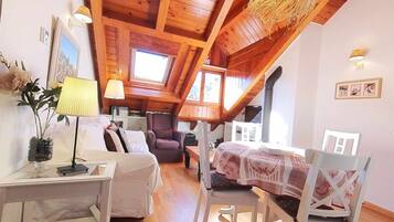 Acogedor dormitorio en ático con vigas de madera, una mesa de comedor, sillas, un sofá y una lámpara.