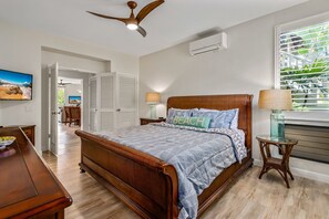 A bedroom with a wooden bed, a ceiling fan, an air conditioning unit, a window with blinds, and a view of the outdoors. - Grand Champions Villas 125, AC, King size Bed, close to Maui's best beaches! (Wailea-Makena)