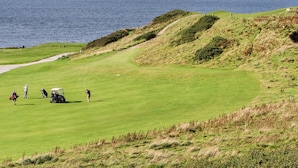 Un parcours de golf avec vue sur la mer, un sentier pédestre et quelques personnes ainsi que des voiturettes de golf.