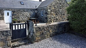 Un bâtiment en pierre avec une porte blanche, un banc et une table à l’extérieur.