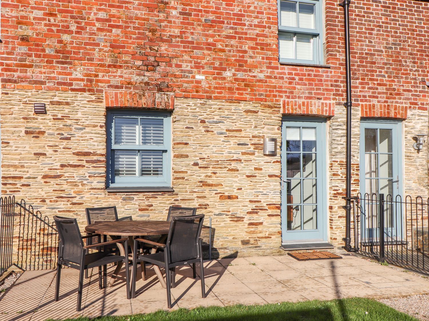 Un bâtiment en briques avec une façade en pierre, une table en bois avec des chaises et une porte bleue.