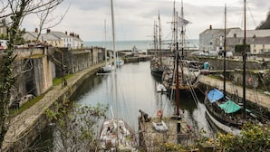 A harbor with multiple sailing boats docked, a stone wall, and buildings along the waterfront. - The Old Smokehouse (St Austell)
