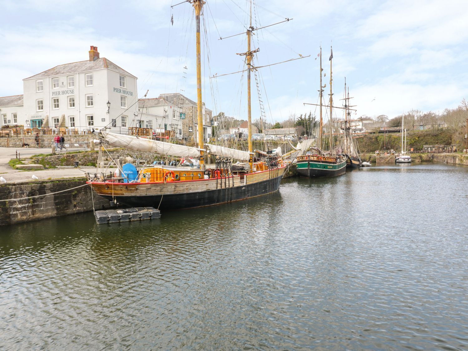 A harbor with several sailing ships docked, a pier house, and a building with a sign.