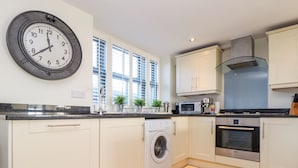 A modern kitchen with white cabinets, a built-in washing machine, a microwave, and a Bosch oven. - The Old Smokehouse (St Austell)