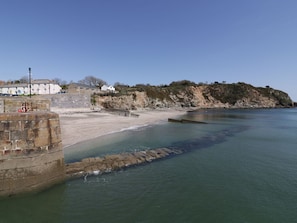 A coastal scene with a stone wall, a sandy beach, and a rocky cliff. - The Old Smokehouse (St Austell)