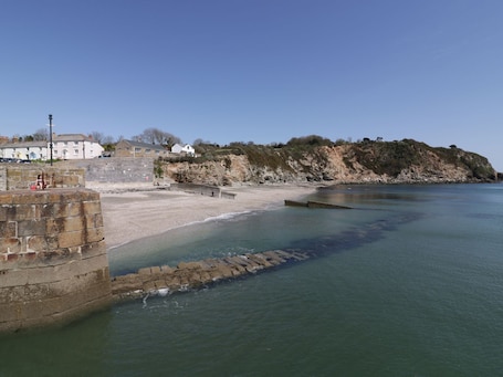 A coastal scene with a stone wall, a sandy beach, and a rocky cliff.