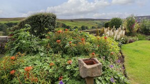 A garden with a stone birdbath, lush greenery, and a view of rolling hills in the background. - Sarah's Cottage (Keighley)